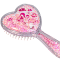 A heart-shaped handheld hairbrush filled with pink glitter and small star-shaped confetti